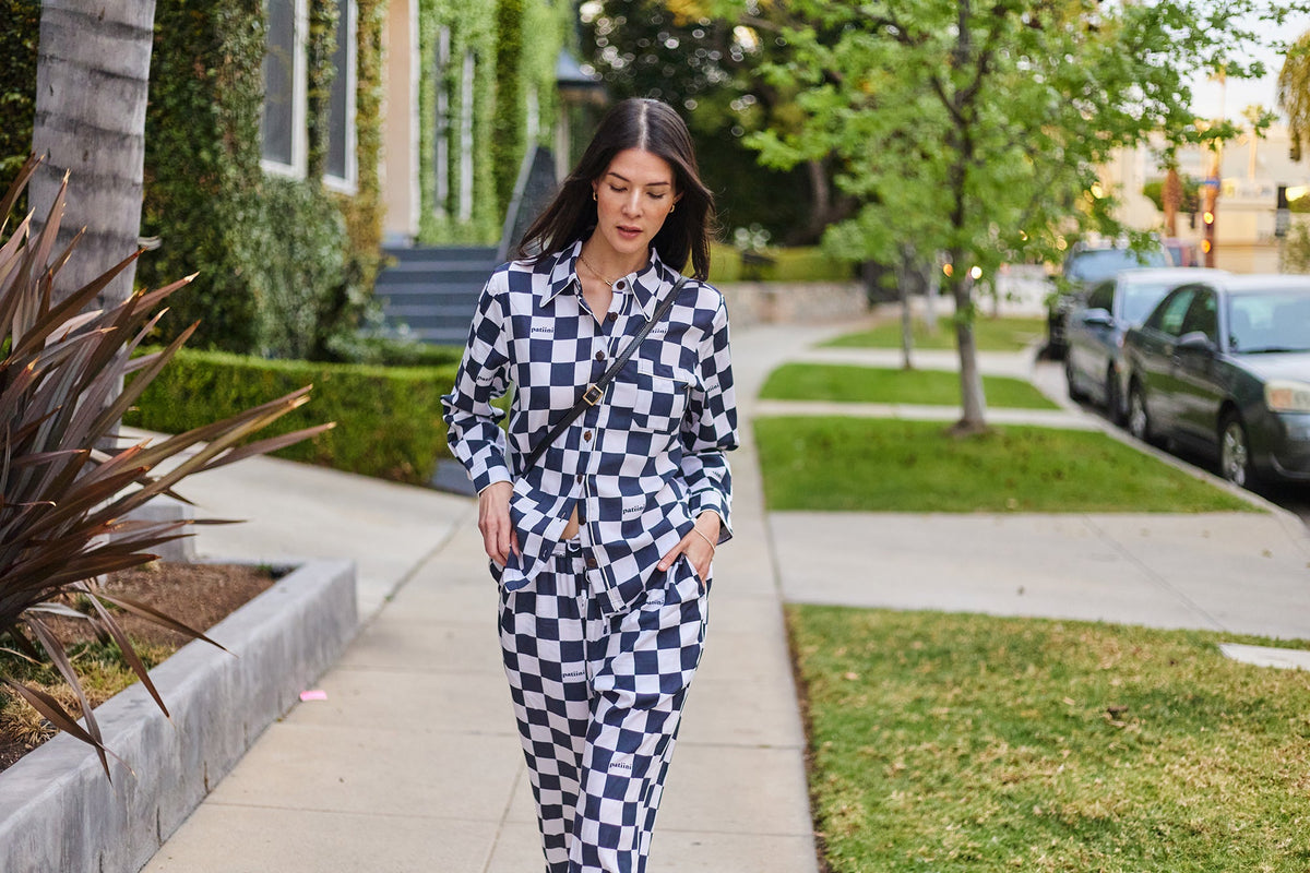 Woman walks down the sidewalk wearing a black and white checkered pajama set.