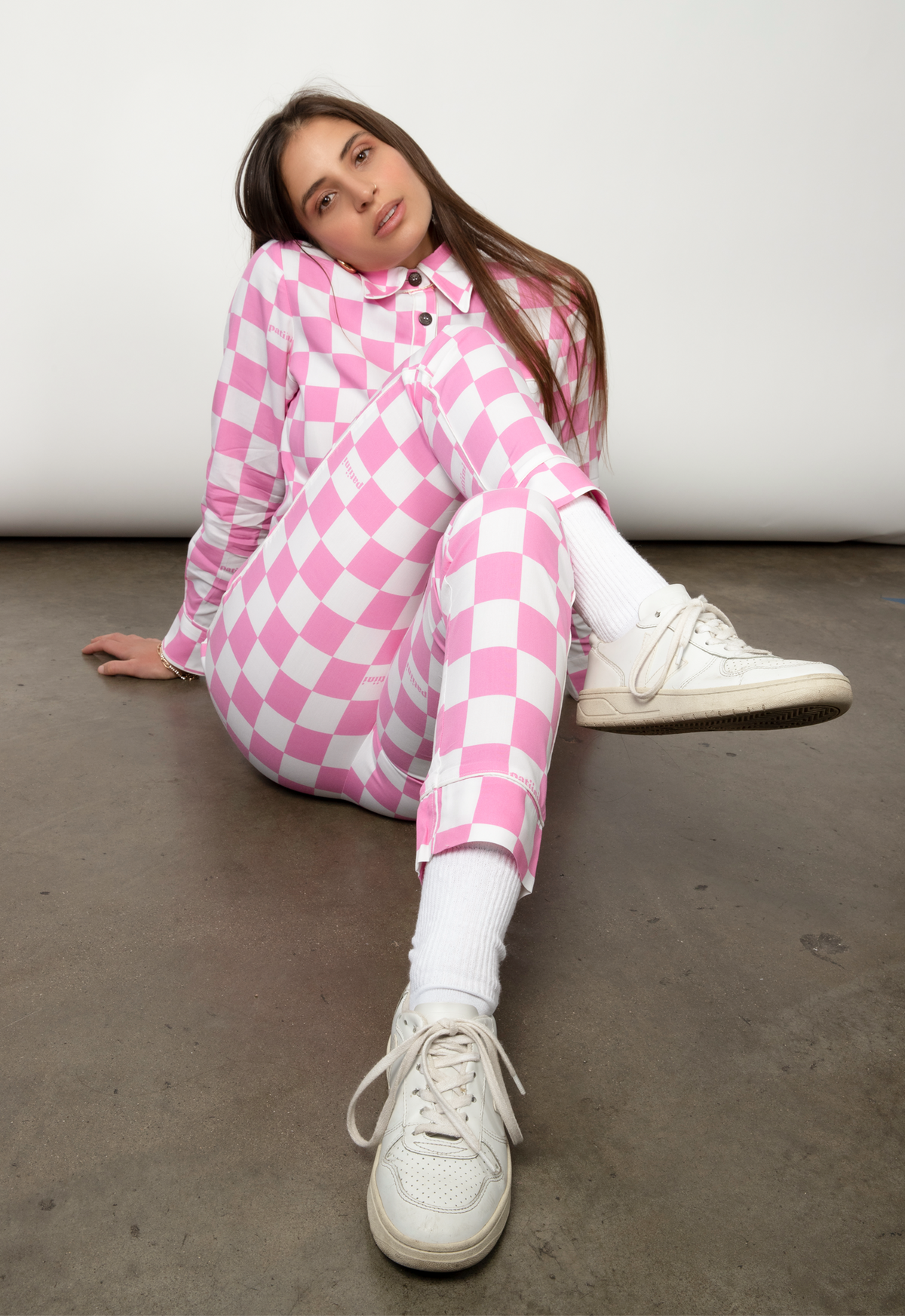 Woman lounges in a pink and which checkered long-sleeve pajama set.