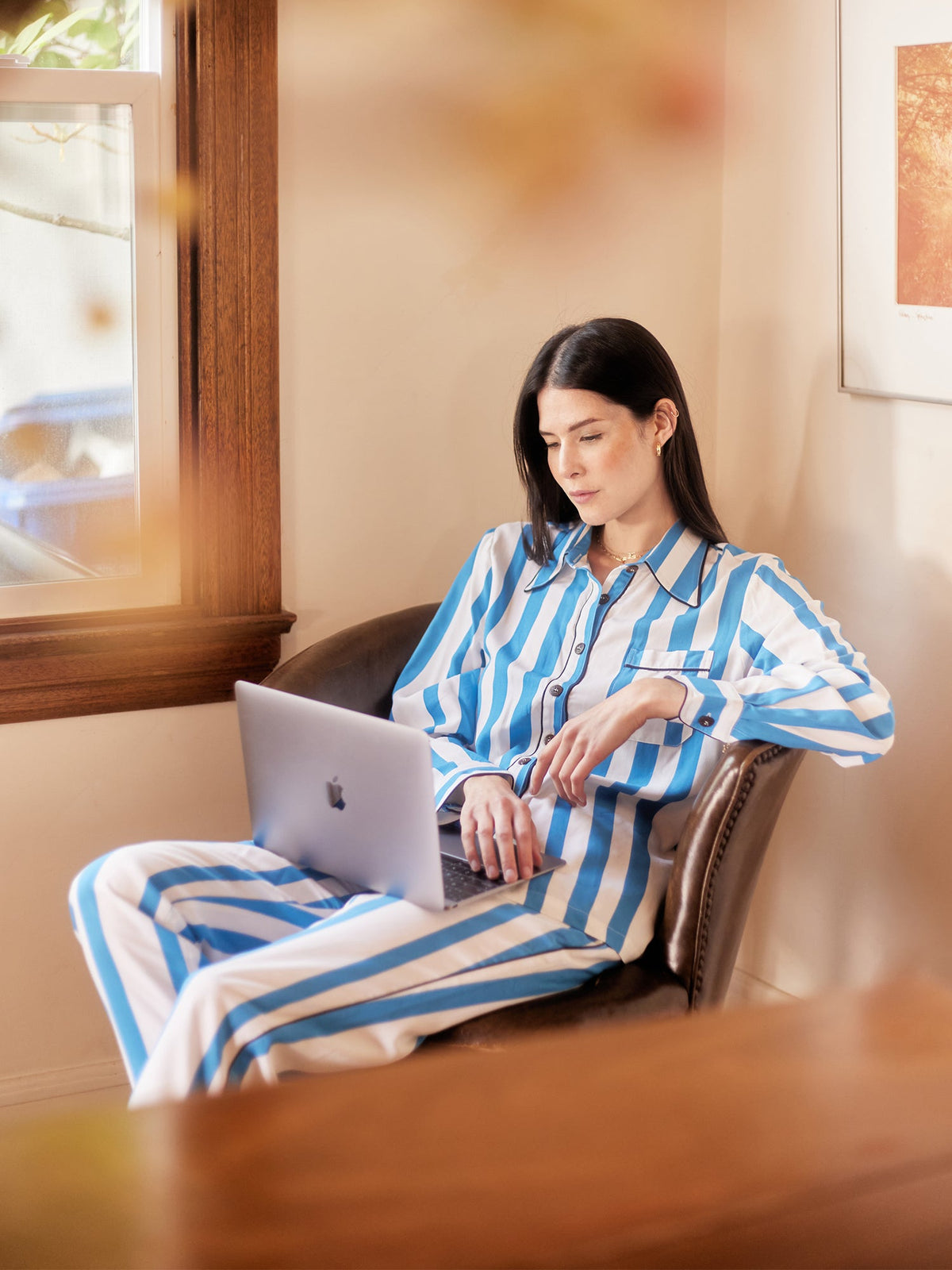 Woman in a blue and white striped long-sleeve pajama set works on her laptop.