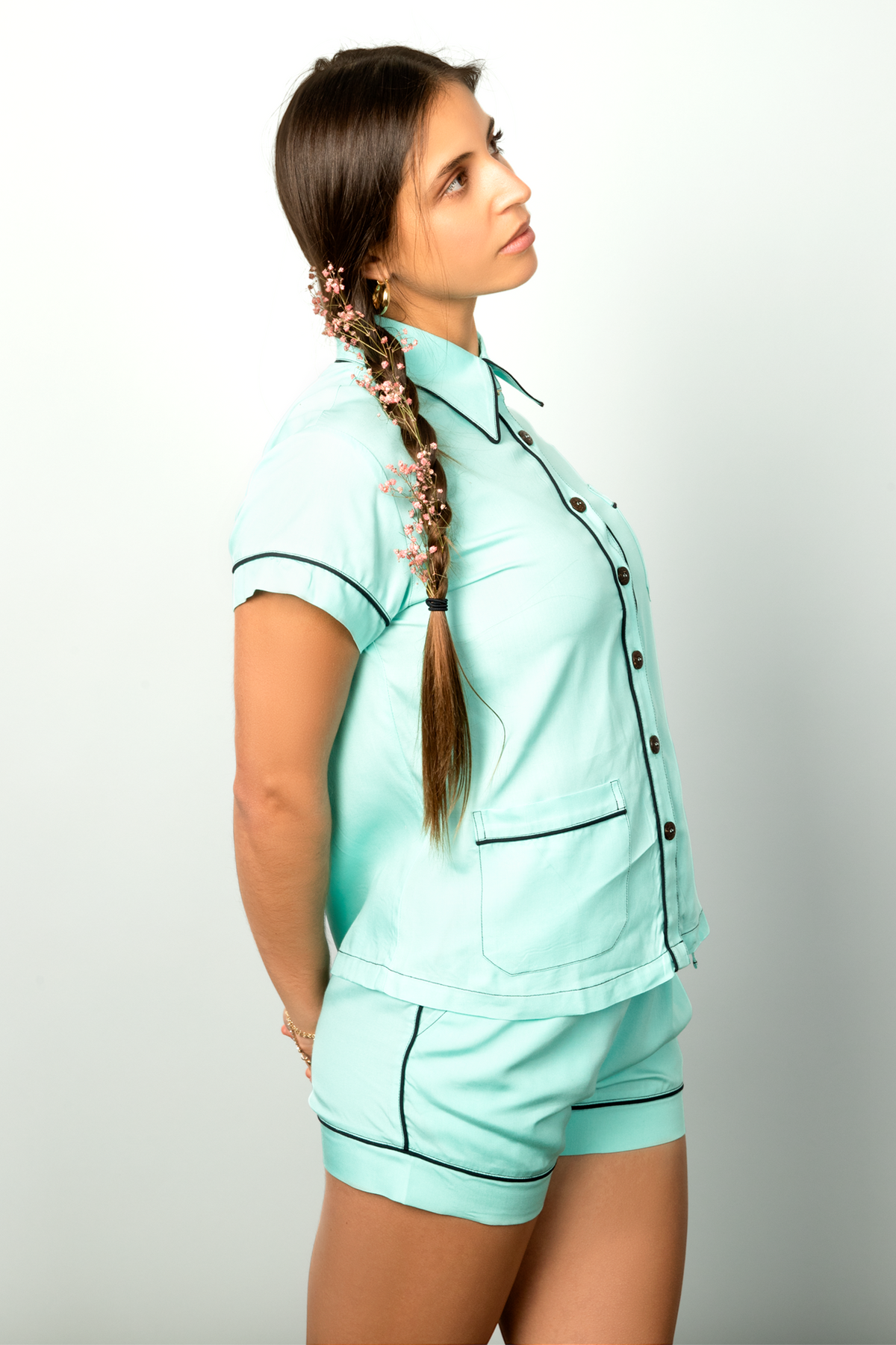 Woman with flowers in her braided hair wears a teal short-sleeve button-down.