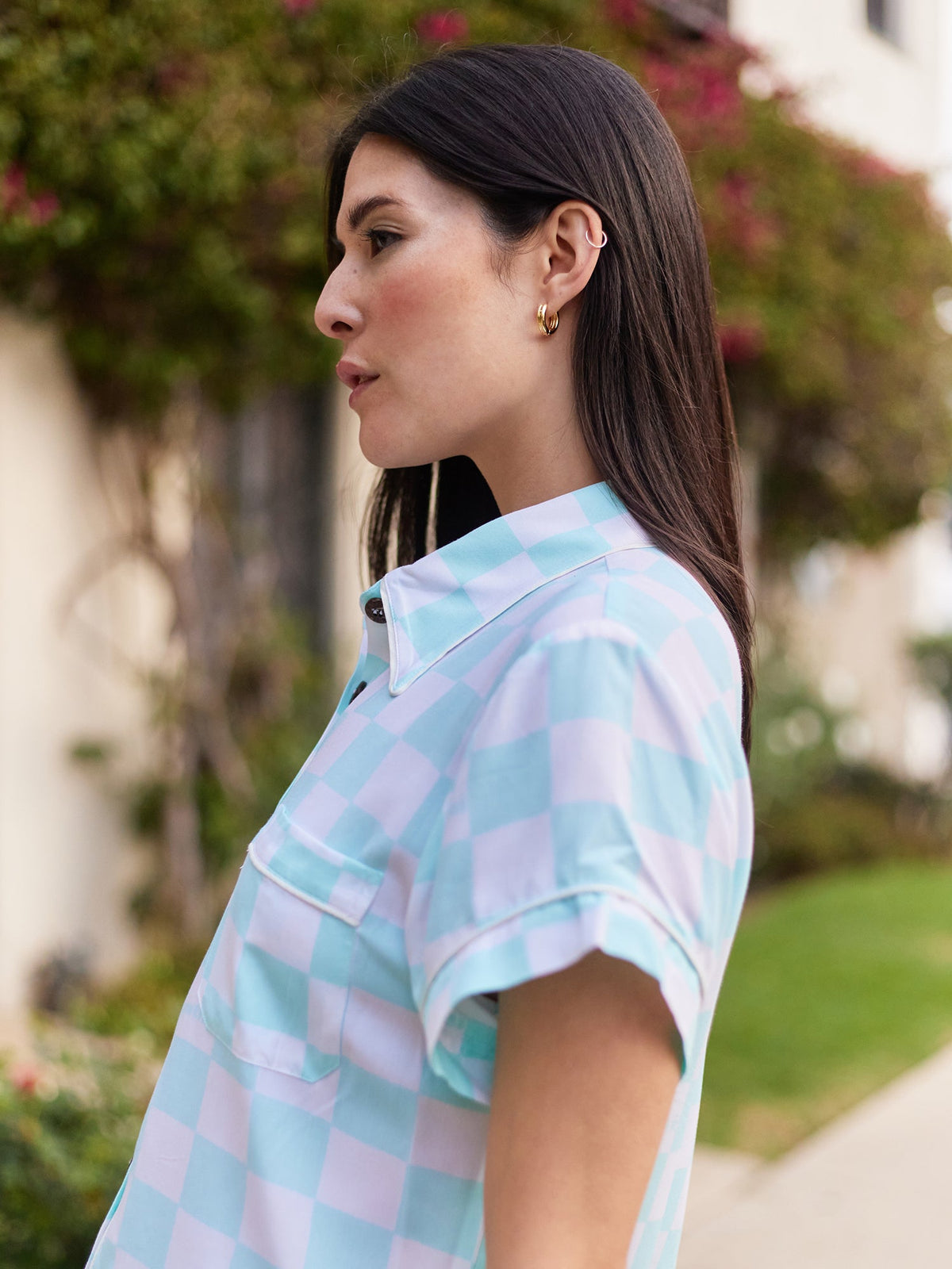 Image of a woman&#39;s profile while she stands on a sidewalk wearing a teal and white checkered checkered shirt.
