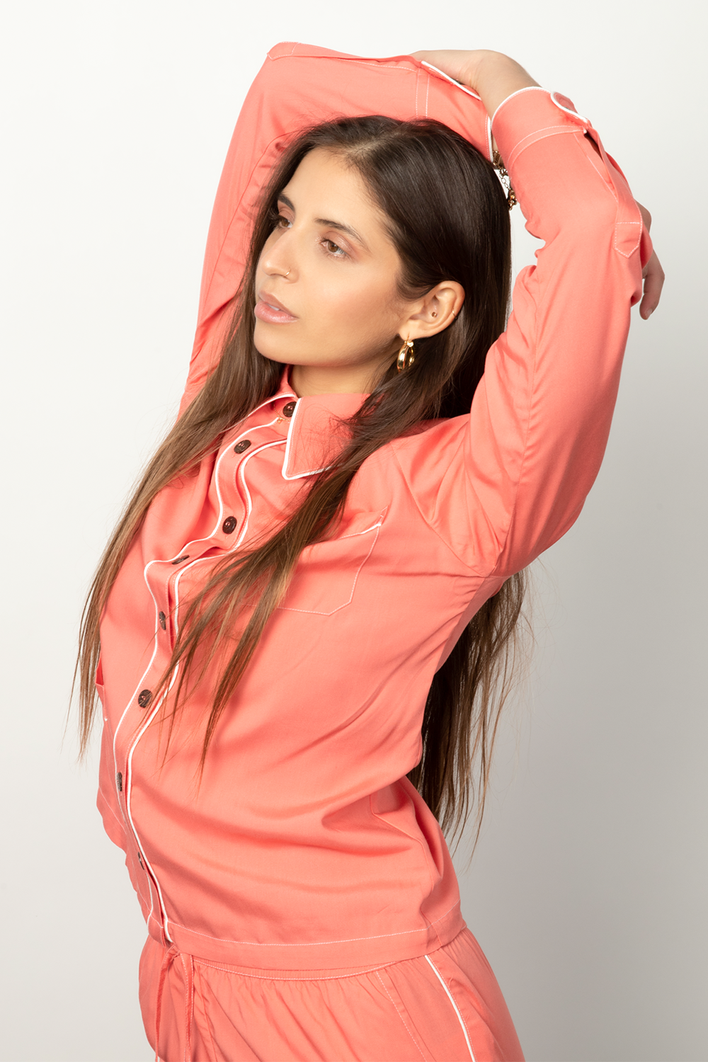 Woman stretches wearing a coral button-down pajama shirt.